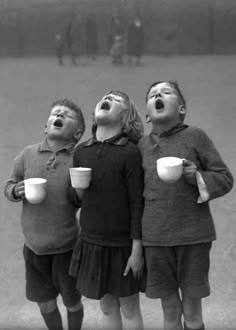 three children with their mouths open while drinking from mugs and looking up at the sky