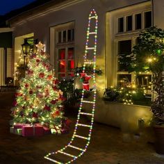 a lighted christmas tree in front of a house with a ladder on the ground next to it