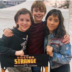 three young children posing for a photo in front of a snow covered slope with the words doctor strange written on it