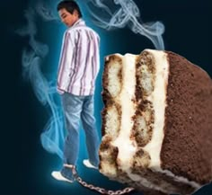 a man standing next to a piece of cake with white frosting on it and a chain