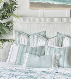 a bed with blue and white pillows on top of it next to a potted plant