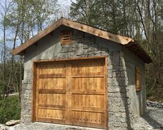 a garage made out of stone and wood with two doors on each side, surrounded by trees