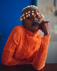 a woman in an orange top sitting at a table with her hand on her chin