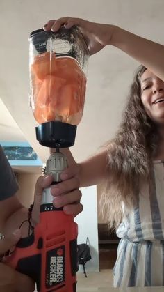 a woman is holding a blender with orange juice in it while another person holds the blender over her head