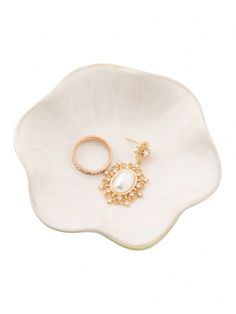 a white flower shaped dish with two gold rings on the front and one pearl in the middle