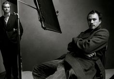 black and white photograph of two men sitting in front of a studio microphone, one with his arms crossed