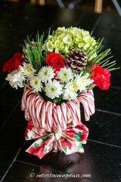 a candy cane with flowers and greenery in it sitting on a table next to a pine cone