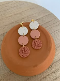 three pairs of pink, white and gold earrings on top of a brown plate with a wooden table