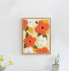 an orange and white flowered painting hangs on the wall next to a potted plant