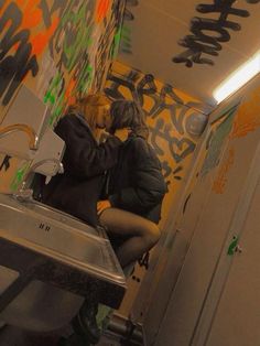 a woman sitting on top of a metal sink in a room with graffiti all over the walls