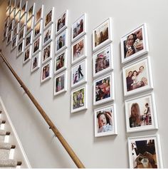 many pictures are hanging on the wall next to some stairs and a wooden hand rail