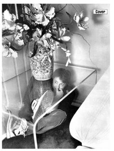 a woman sitting on the floor next to a vase with flowers in it and an open book