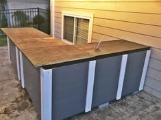 an outdoor swimming pool with a wooden counter top and metal bars on the bottom, in front of a house