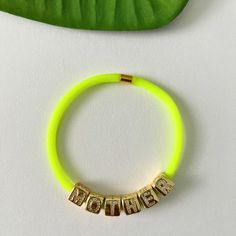 "Gift your mom this sleek neon yellow bracelet that is uniquely handmade with rubber/silicone tube. Rubber tube bracelets are water-proof and feel comfortable on your skin. Each bracelet is tastefully finished with a high quality, tarnish-free, matte gold end cap that also doubles as a clasp.  Each bracelet includes the word \"MOTHER\" spelled out in 18K gold plated, cube initial charms engraved with micro pave stones. If you need different charms, please check my listing for charms here: https://www.etsy.com/listing/1462738336/ Bracelet length- You can select a length from 6-9 inches. Please DM if you need a custom size and I will make it for you. Bracelet thickness-4mm Charm size- 9mm x 8.5mm This bracelet is also available in purple, lime green, tangerine and hot pink/fuchsia. Please ch