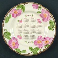 a white plate with pink flowers and green leaves on the rim, which has a calendar for each month