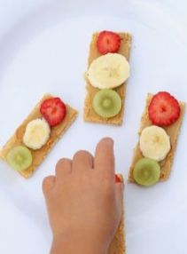 a person reaching for some fruit on top of crackers with kiwis and strawberries