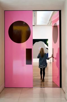 a woman walking into a room with pink and brown doors that have circles on them