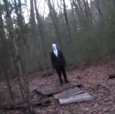 a person standing in the woods wearing a black suit and white mask with trees behind them