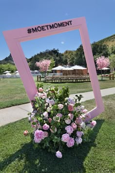 a pink frame with flowers in it sitting on the grass next to a sign that says mootmoment