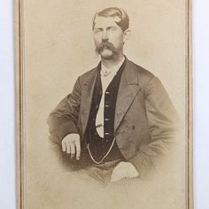 an old photo of a man with a mustache and suit jacket sitting in front of a white wall