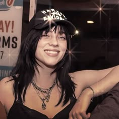 a woman with long hair wearing a baseball cap and smiling at the camera while standing in front of a sign that says happy birthday