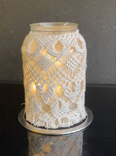 a white crocheted candle holder sitting on top of a black table next to a wall