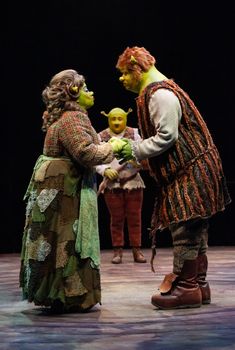 two people dressed in costumes standing next to each other on a stage with one holding a doll