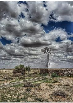 a windmill sitting in the middle of a dry grass field under a cloudy blue sky