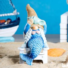 a figurine of a mermaid sitting on top of a white bench in the sand