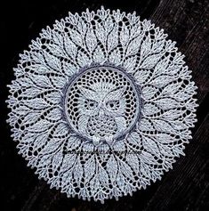 a crocheted doily with an owl in the center on a wooden surface