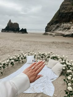 a person holding their hand out to someone laying on the beach with flowers in front of them