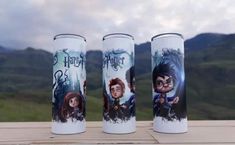 three harry potter tumbles sitting on top of a wooden table with mountains in the background