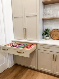 an open drawer in the middle of a kitchen with white cabinets and wood flooring