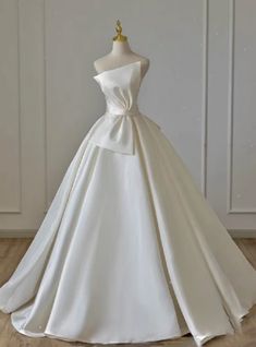 a white wedding dress on a mannequin stand in front of a wall and wooden floor