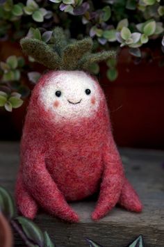 a red stuffed animal sitting next to a potted plant with leaves on it's head