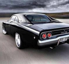 an old black car driving down the road with dark clouds in the sky behind it