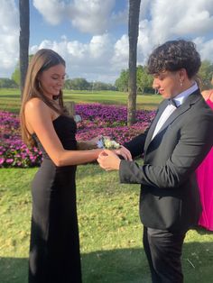 a man in a tuxedo is handing flowers to a woman in a black dress