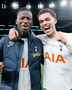 two men standing next to each other on a soccer field with lights in the background