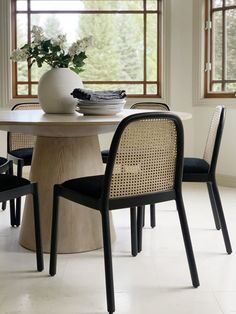 a dining room table with four chairs and a vase on the table in front of it