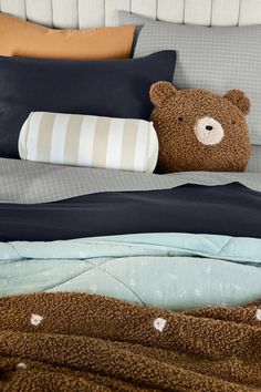 a brown teddy bear sitting on top of a bed next to pillows and blankets in a bedroom