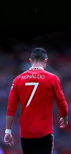 a man in red jersey standing on soccer field with his back turned to the camera