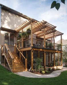 a large house with wooden stairs and plants on the balconies, surrounded by green grass