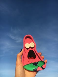 a hand holding a pink spongebob cell phone case in front of a blue sky