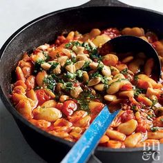 a skillet filled with pasta and vegetables on top of a table next to a blue spoon