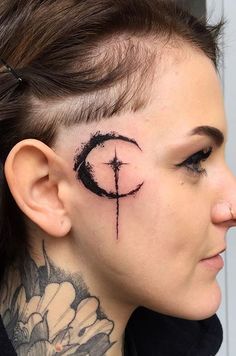 a woman with black ink on her face and behind her ear is a cross tattoo