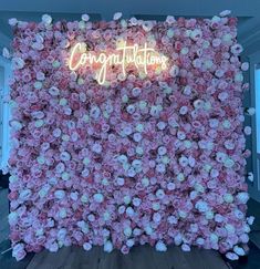 a pink flower wall with the words congratulations written on it in neon lights and flowers