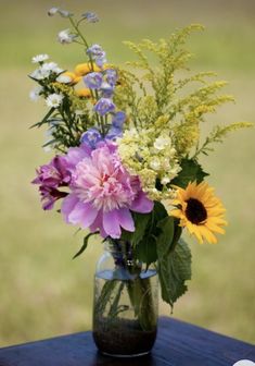 a vase filled with lots of flowers on top of a wooden table next to grass