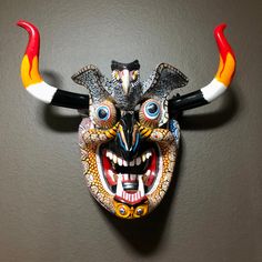 "Large Mexican Decorative Indigenous Diablo Wall Mask.  Handcrafted from Copal wood from Michoacán, Mexico. Hand carved and hand painted with bright colors and intricate designs. Signed by artist.  Approx. 18\" x 14\" x 7\" (w x h x d) Each artisan wall mask is unique. This one depicts a colorful diablo skull. Since these are hand painted and hand crafted, slight imperfections may exist. Each one is one of a kind. We ship these masks with the horns removed for safe delivery. Horns should be tied together in the back after assembly. Any mask lovers out there? We're excited to bring in some amazing hand carved copal wood masks from Tócuaro, Michoacán, México. The colors and intricate details are amazing. These are as authentic as you can get. The larger masks take over a month to complete. F Mexican Mask, Manitou Springs, Wall Mask, Home Workshop, Arte Popular, Clay Masks, Mexican Folk Art, Hand Carved Wood, Intricate Designs