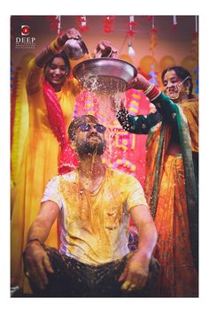 the man is pouring water on his face and other people are standing around him, all dressed in bright colored clothing