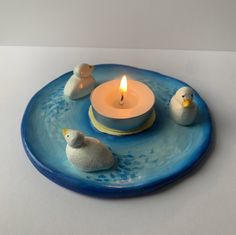 three ducks sitting on a blue plate with a lit candle